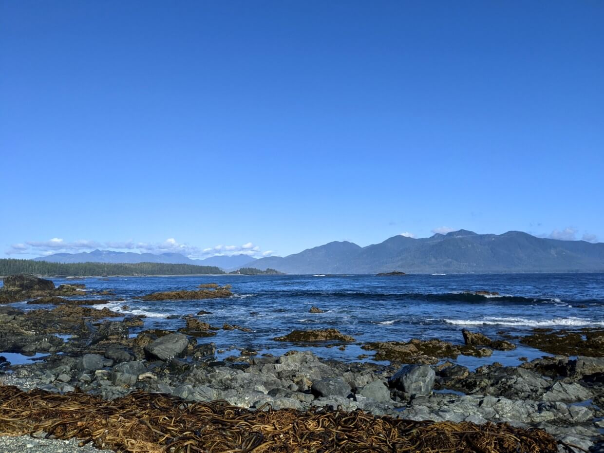 Looking across rocky shoreline and the ocean to Yuquot and Vancouver Island mountains from the Nootka Trail