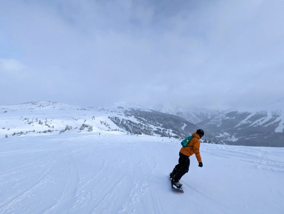 Back view of JR snowboarding at Sunshine Village Resort in Alberta, with snowy hills opposite