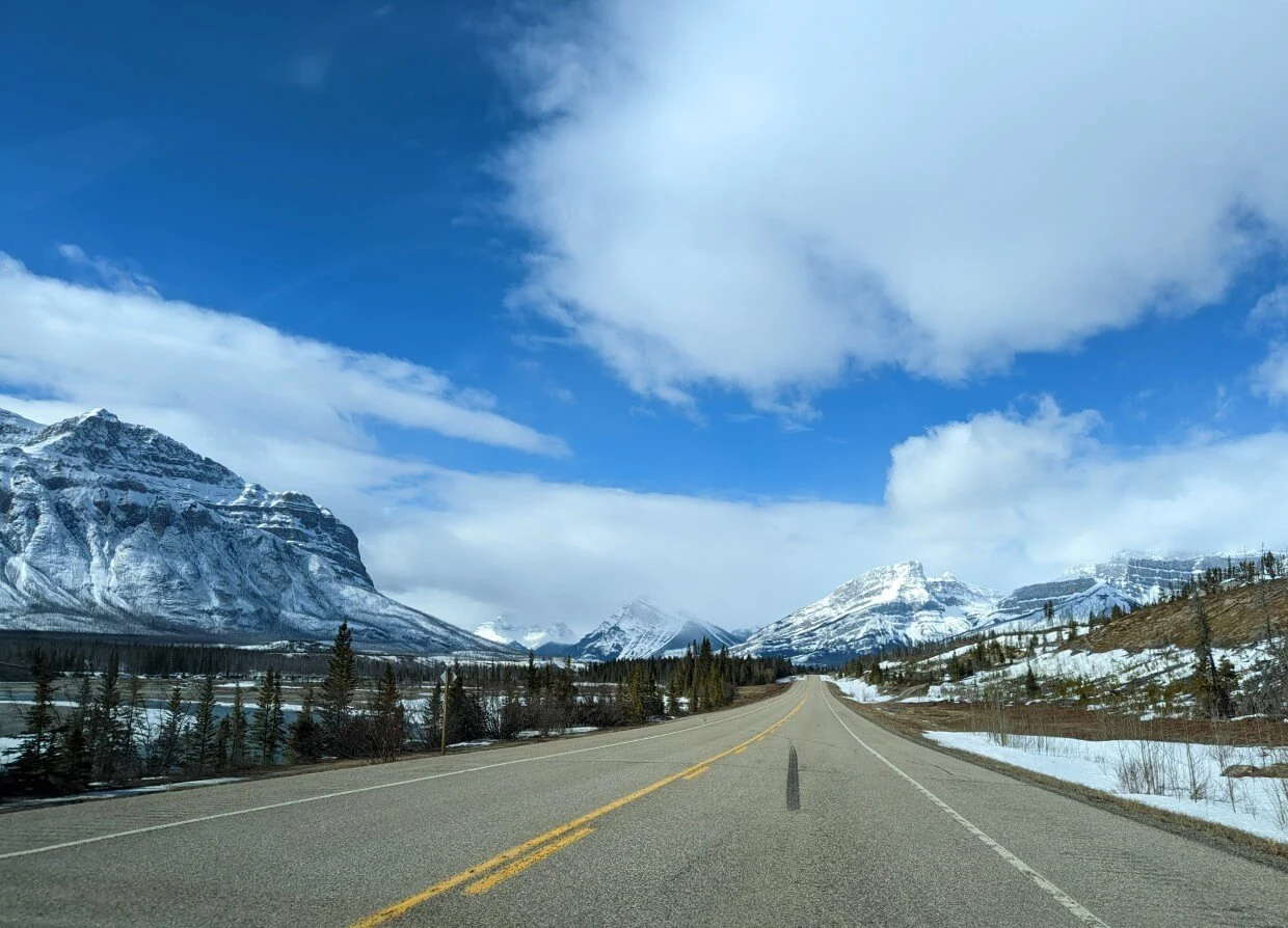 Driving the David Thompson Highway in Canada, vehicle view. The clear road is surrounded by snowy mountains