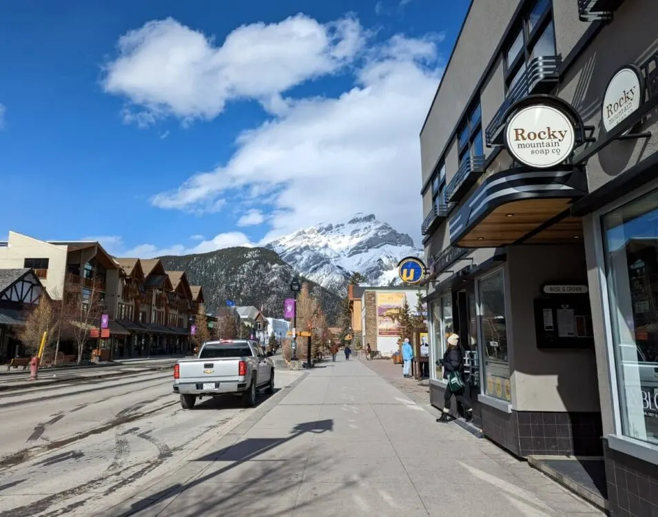 Looking down street in Banff, with stores on right and across the road to the left, and snowy Cascade Mountain in background