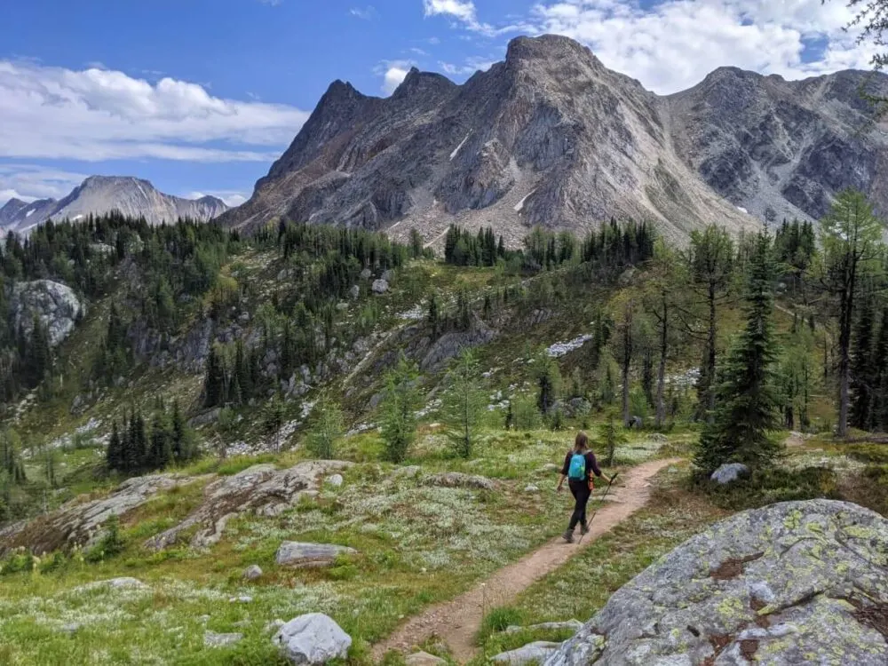 Back view of Gemma walking away on Jumbo Pass Trail, which is backdropped by Bastille Mountain and subalpine meadows
