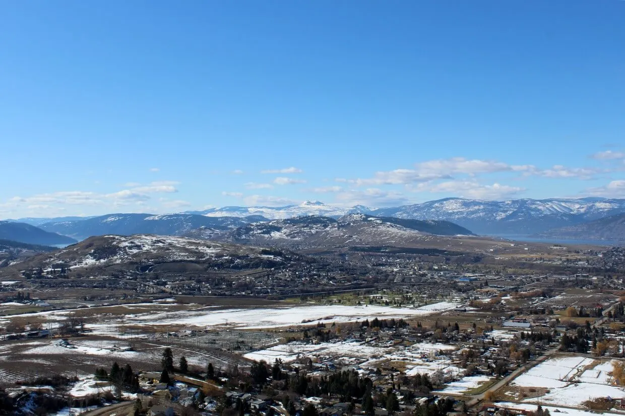 Looking across partially snow covered landscape in Vernon with snow capped mountains in background