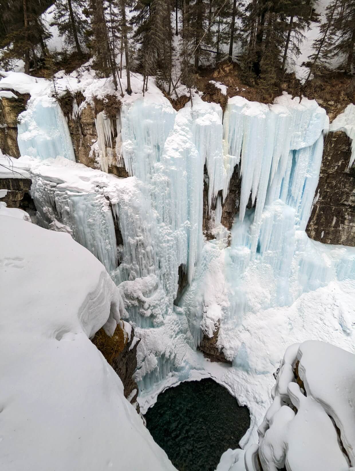 Huge frozen waterfall with many icicles on edge of canyon, with water visible at bottom, Johnston Canyon