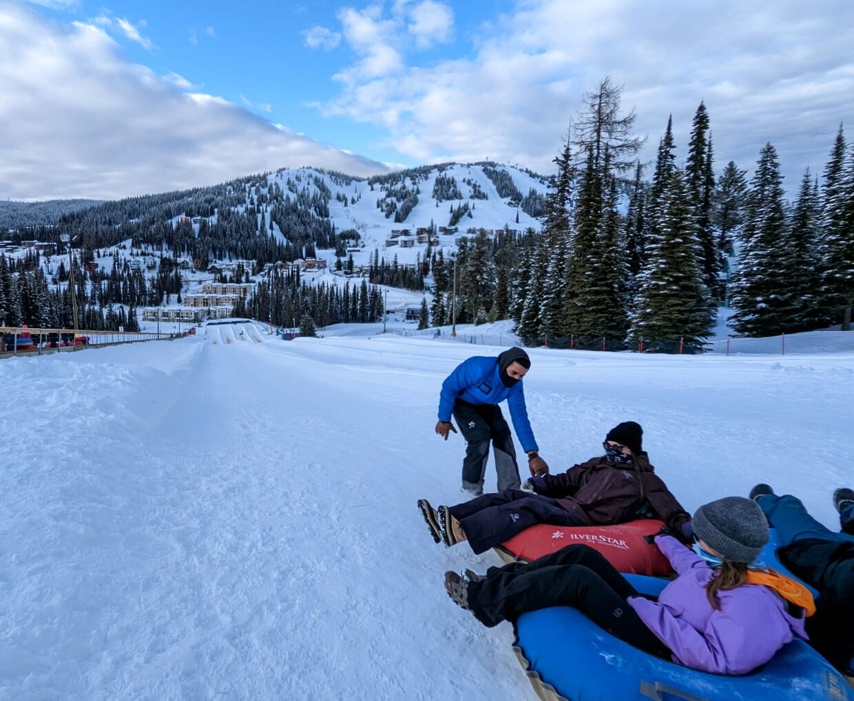 Three people sit in snow tubes waiting to slide down frozen slope at Silver Star Ski Resort