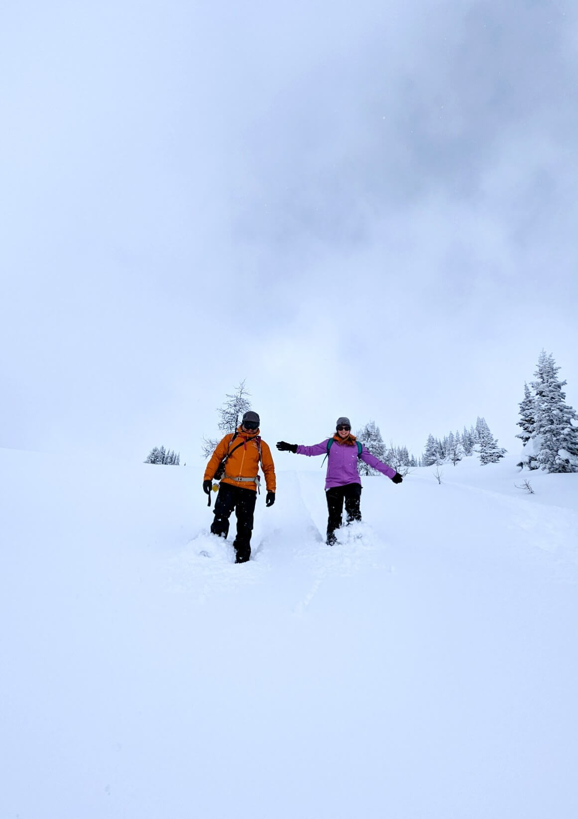 Gemma and JR run towards the camera through snow wearing colourful waterproof jackets