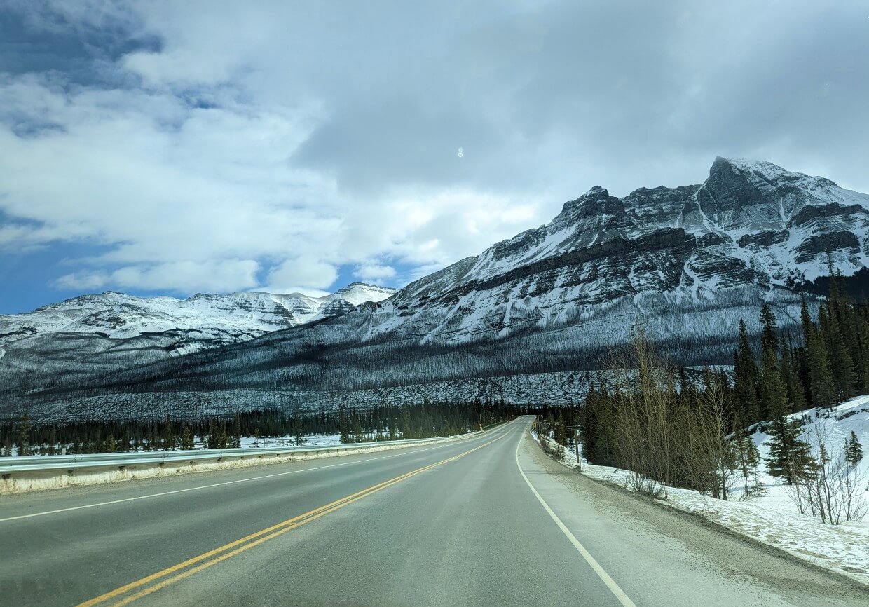 Vehicle view of Alberta road in winter, with snow covered mountains in front