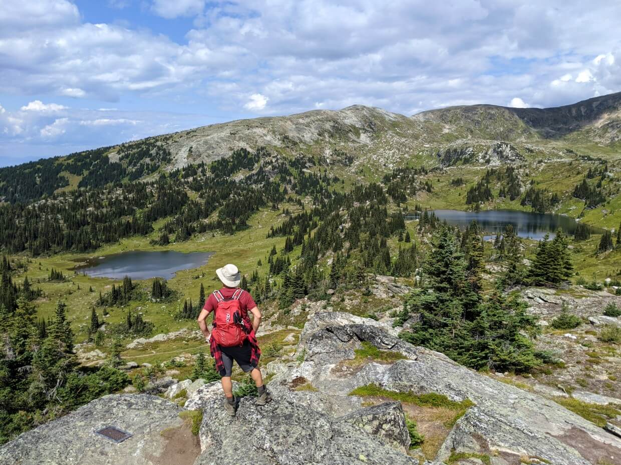 Back view of JR standing on rock looking out to alpine lakes on Trophy Meadows Trail