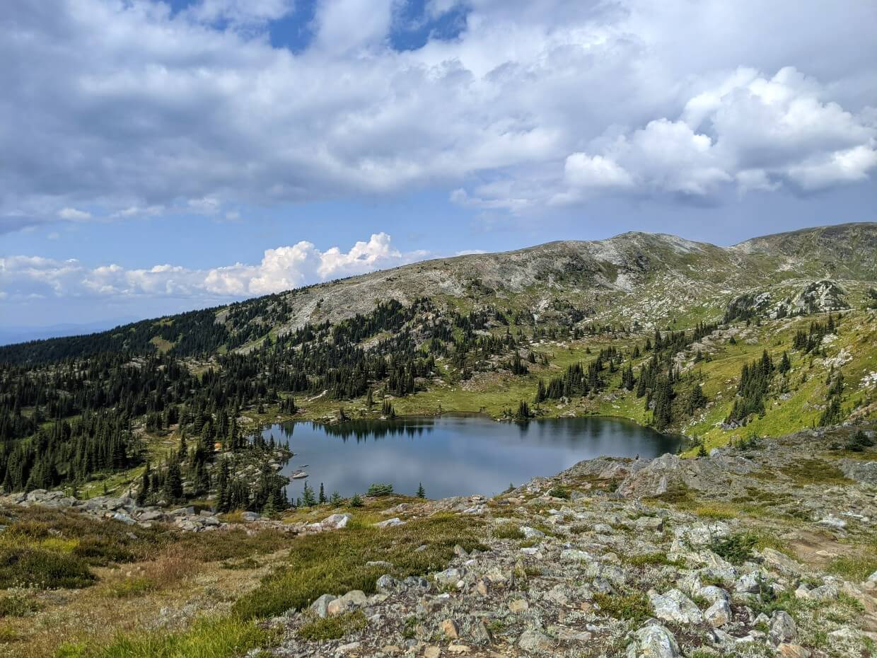 Elevated view looking down to calm Sheila Lake, which sits in a sub-alpine bowl, partially surrounded b trees