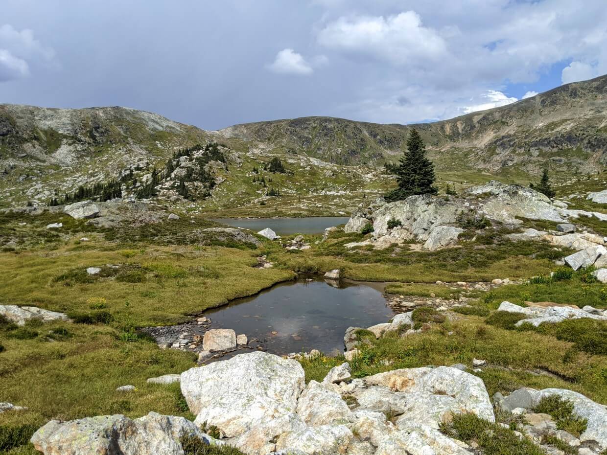 Small alpine tarns with scattered rocks and mountain ridge in background, Plateau of the Lakes area on the Trophy Meadows Trail