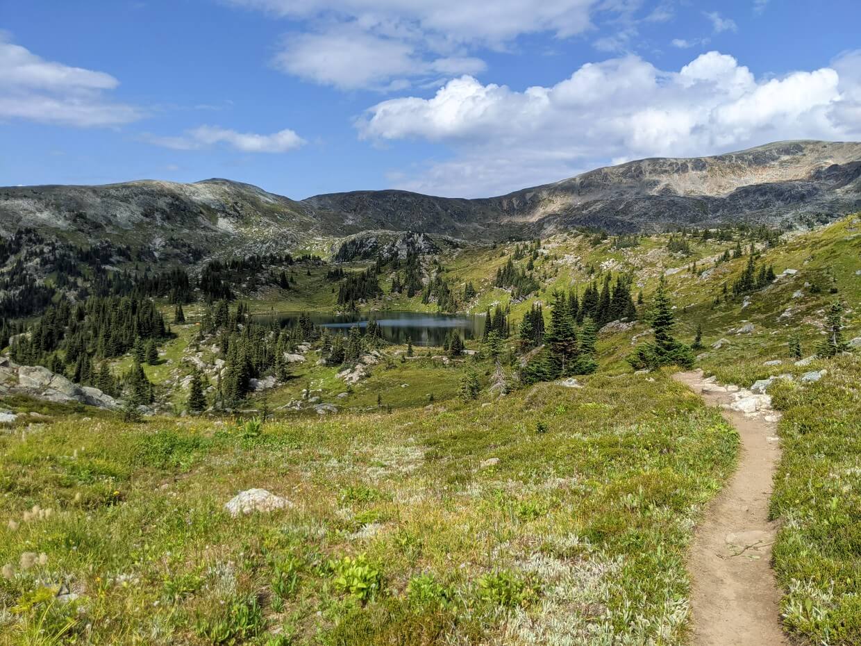 Hiking trail on right hand side leading to calm Sheila Lake in distance, with mountain ridge in background
