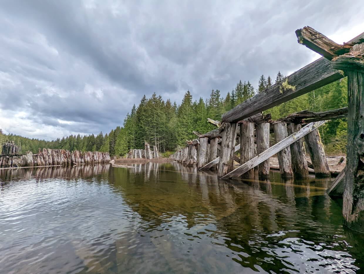 Old railway trestle on Gray Lake that is rotting away. The view is from the water and more wooden boards can be seen in the shallow water.