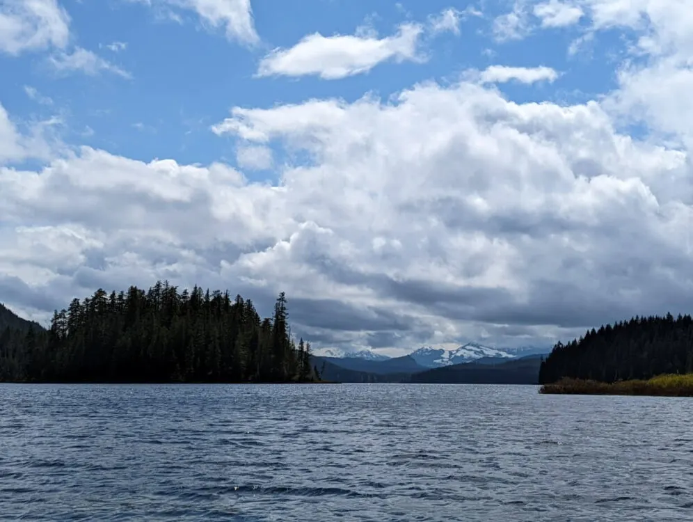 View from Brewster Lake on a cloudy day of the snow capped mountains in the distance.