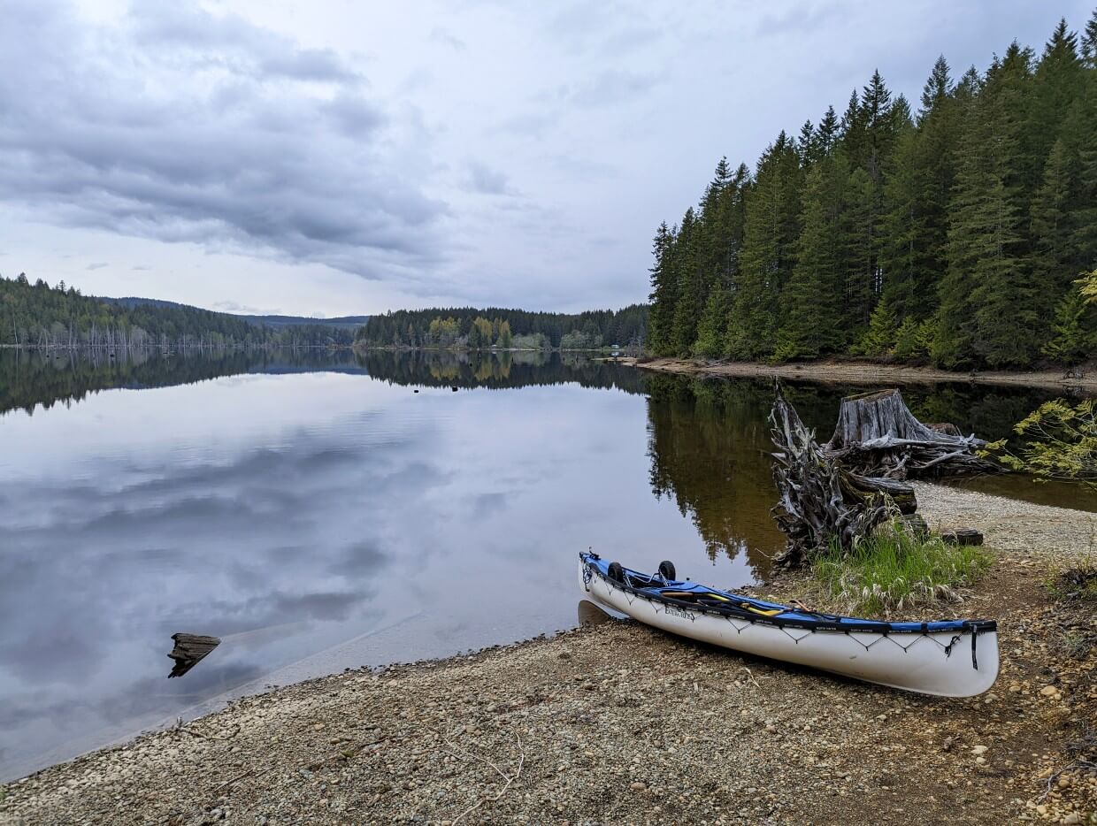 A canoe sits at the edge of Fry Lake. The water is still and reflecting the surrounding forest.