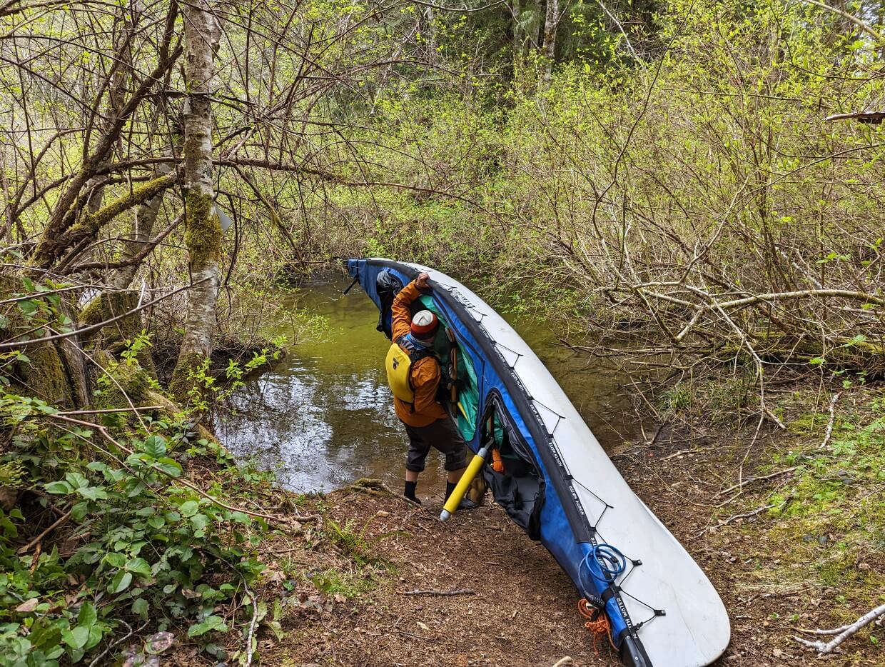 Man launching a canoe into the river. The water is surrounded by dense foliage, including trees and brush.