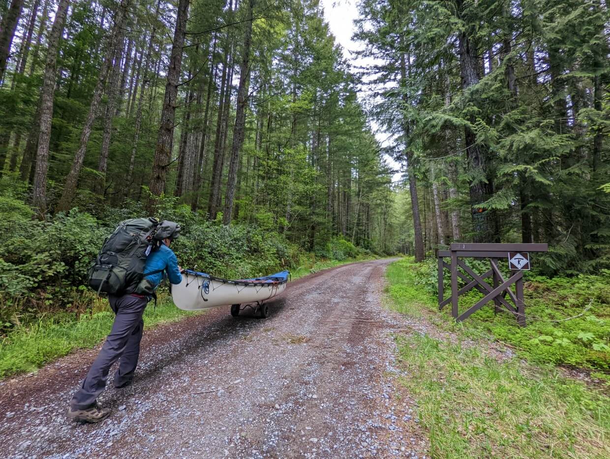 Man portaging between Campbell Lake and Gosling Lake. The trail is uphill by gravel and flanked on both sides by the forest.