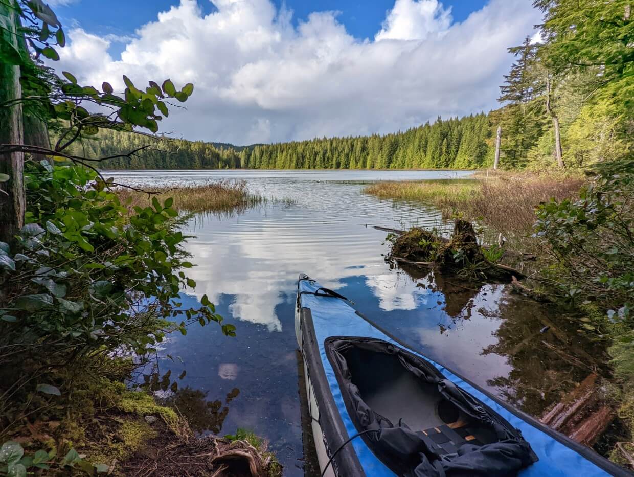 Canoe sitting at the water's edge on Tiny Lawier Lake. The lake has soft ripples and reflecting the blue skies and fluffy white clouds.