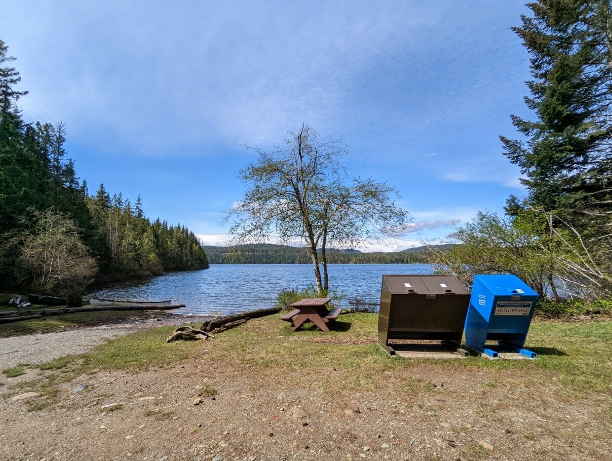 Mohun Lake boat launch in Morton Lake Provincial Park. There is a picnic table on the shore as well as garbage and recycle containers.