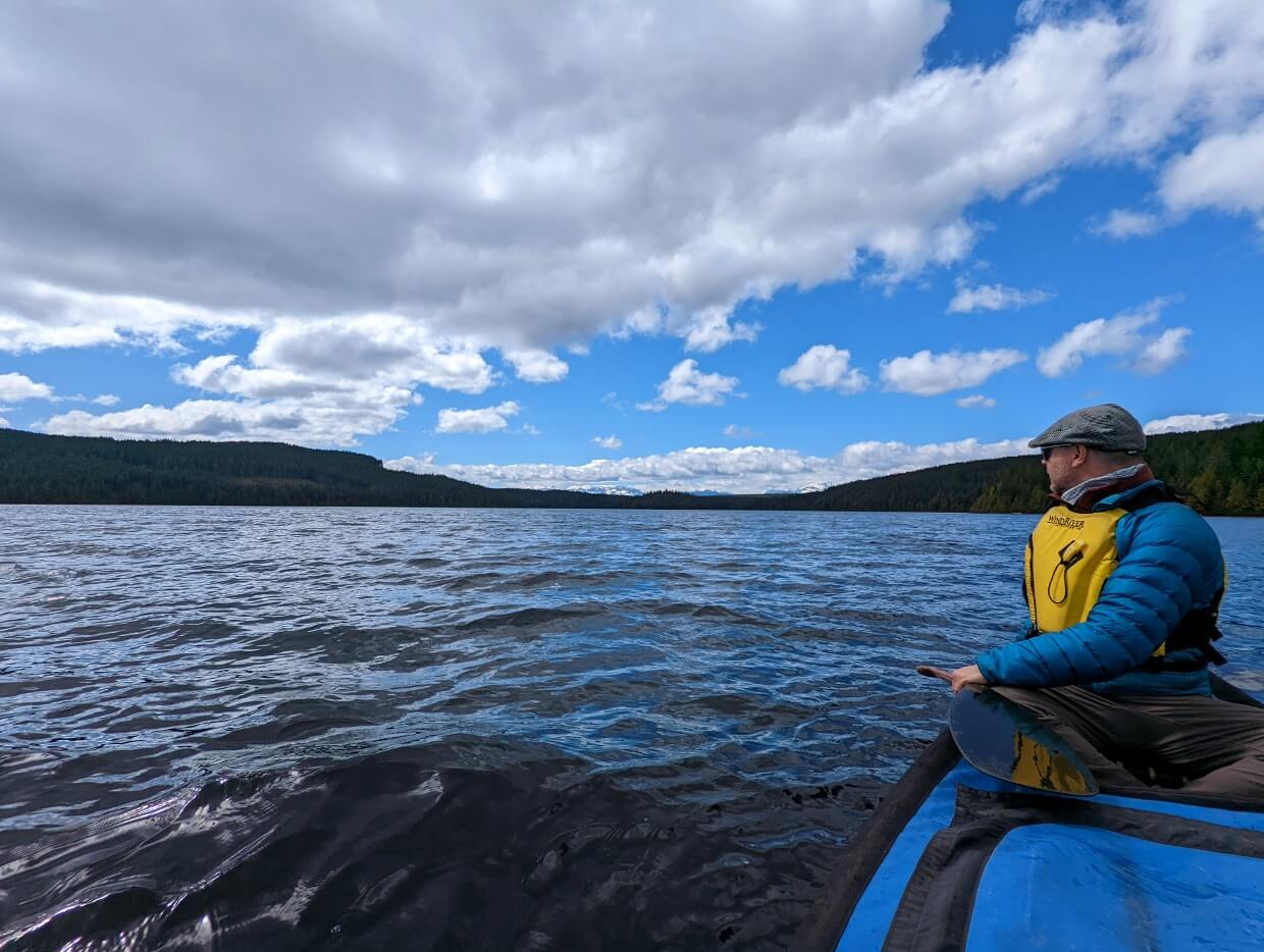 Man paddling in a canoe on Mohun Lake. He's looking back at the view of the mountains in the distance.