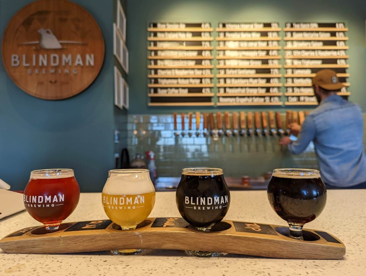 Four beers sit in wooden flight holder on bar counter at Blindman Brewing in Lacombe