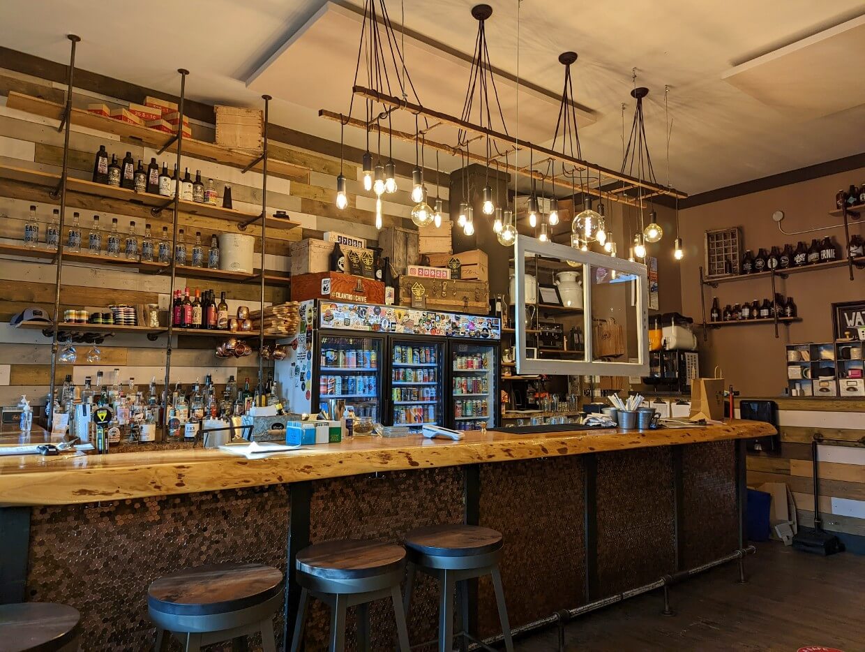 Cilantro and Chive bar with long wooden counter and hanging lighting with large beer fridge behind