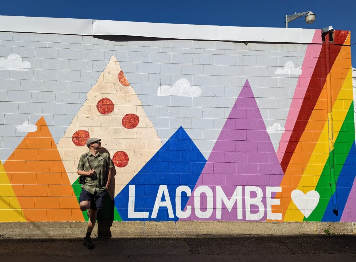 JR is standing in front of a colourful mural with the words Lacombe in capital letters to the right hand side