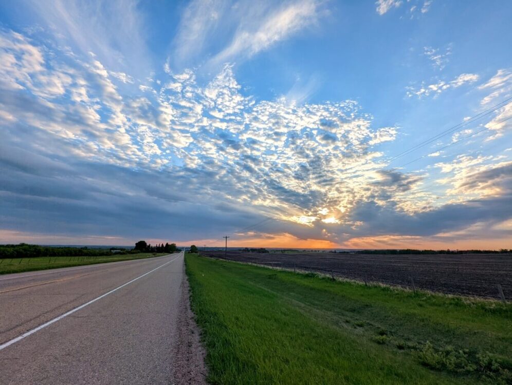 Road view of sunset over Lacombe, with orange colours and scattered clouds