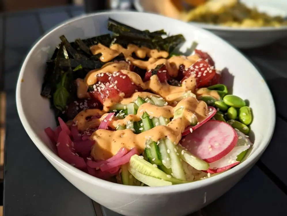 Close up of poke bowl at Tollers Bistro, with vegetables, ahi tuna, seaweed and sriracha sauce in white bowl