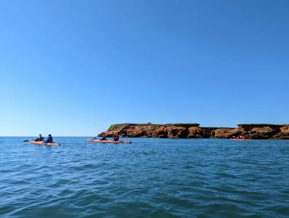 Kayakers in front of red coloured cliffs, on calm ocean