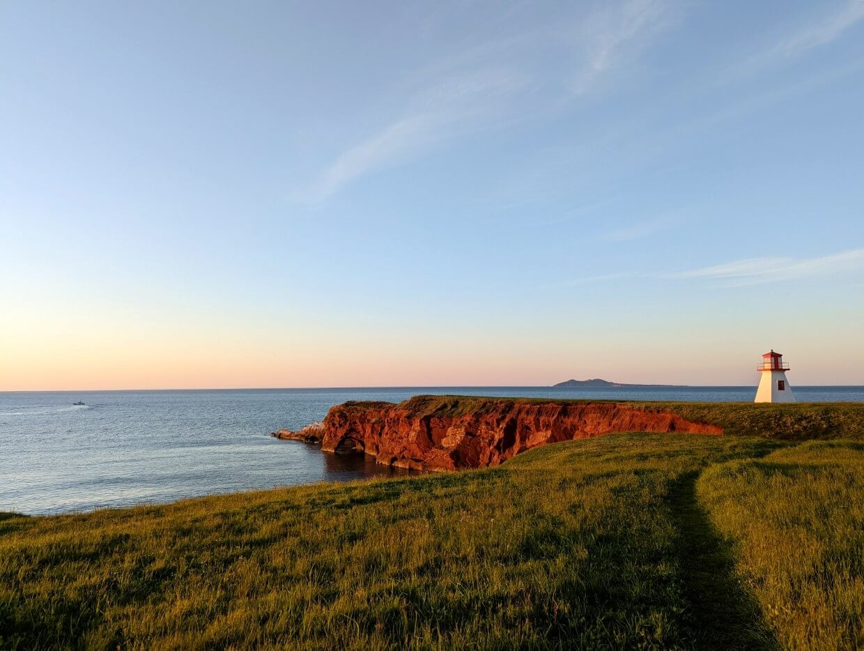Looking ahead to path through the grass at sunrise leading to the red and white lighthouse at Cap Alright on Îles de la Madeleine