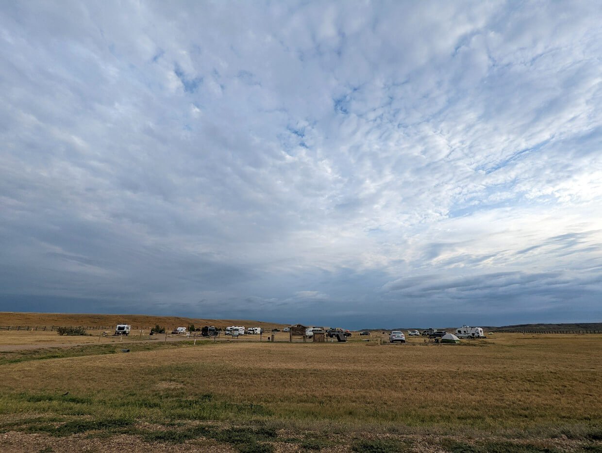 Collection of RVs and cars parked in campsites at Frenchman Valley Campground with big skies above