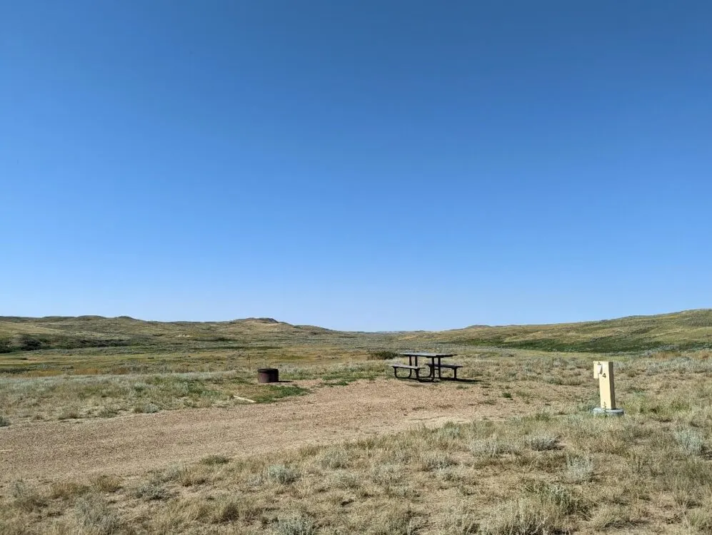 Campsite at Rock Creek Campground, an open dirt area in front of rolling hill scenery with picnic table and fire pit