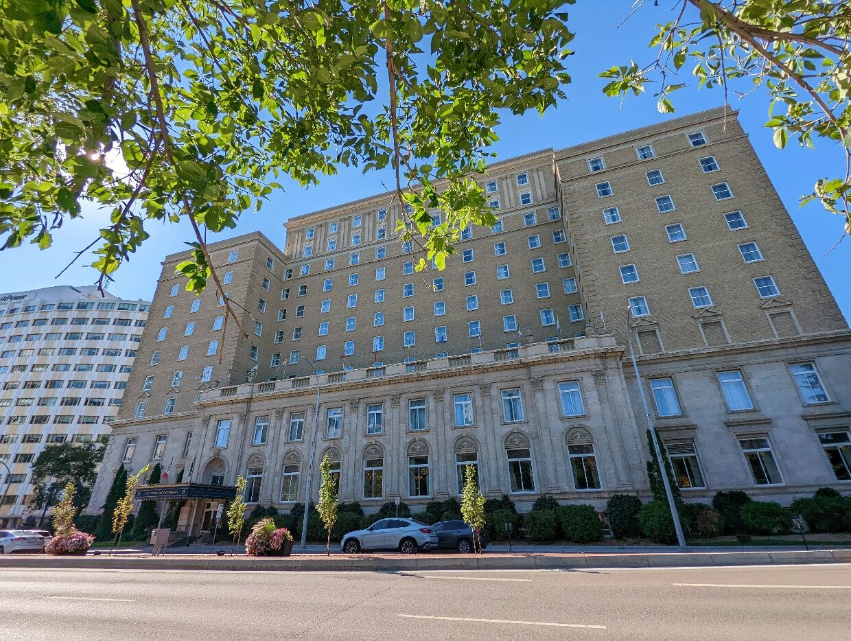 Looking up at the Hotel Saskatchewan, a ten story railway hotel in Regina. Some leaves from the tree above are visible