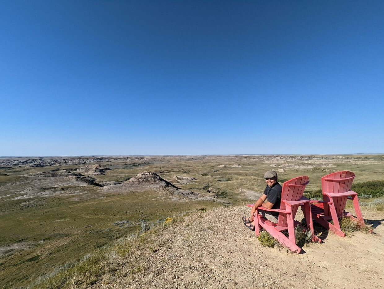 Back view of JR sitting on red Parks Canada Adirondack chair in front of scenic view featuring hoodoos and ravines