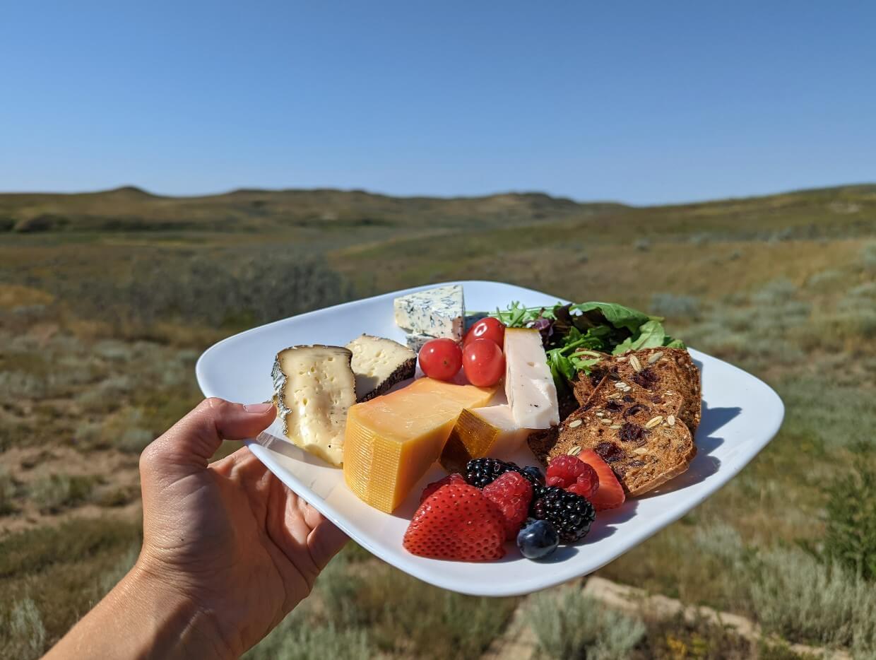 Close up of white lunch plate in front of Grasslands scenery, with cheese, crackers, fruit