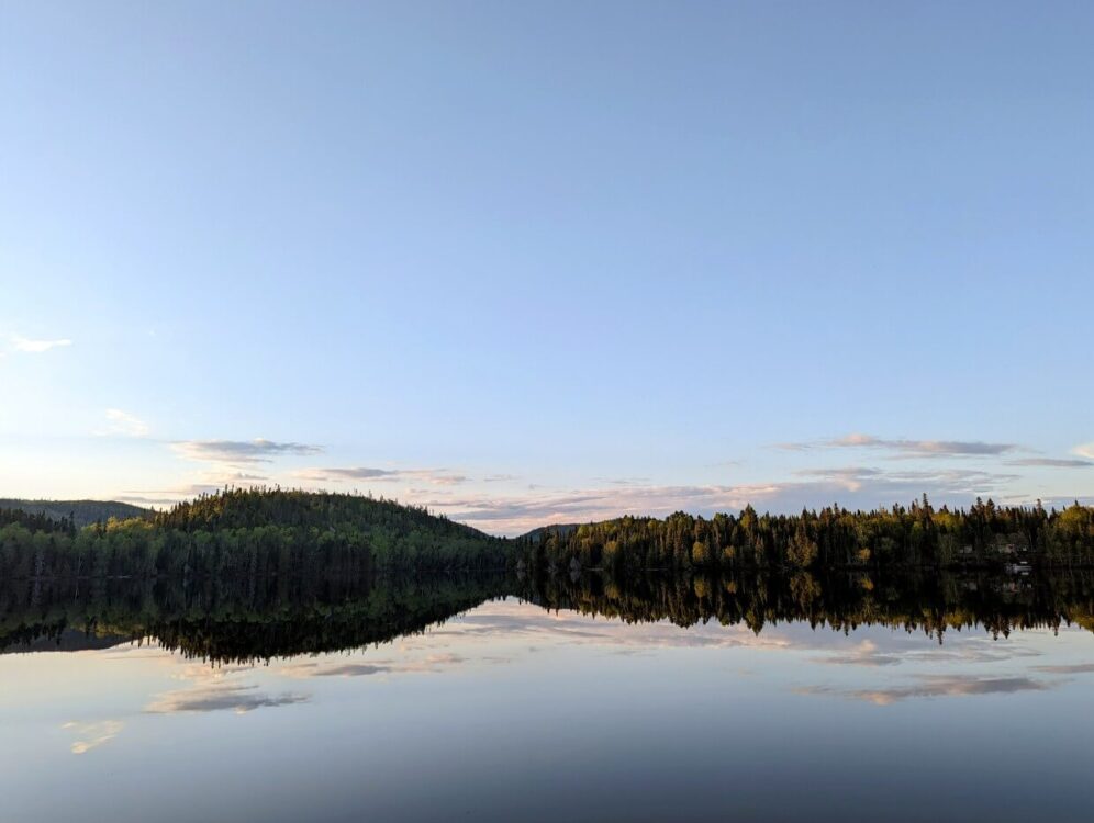 Sunset mirror reflections on Whitesand Lake, with trees and clouds visible on the calm lake surface