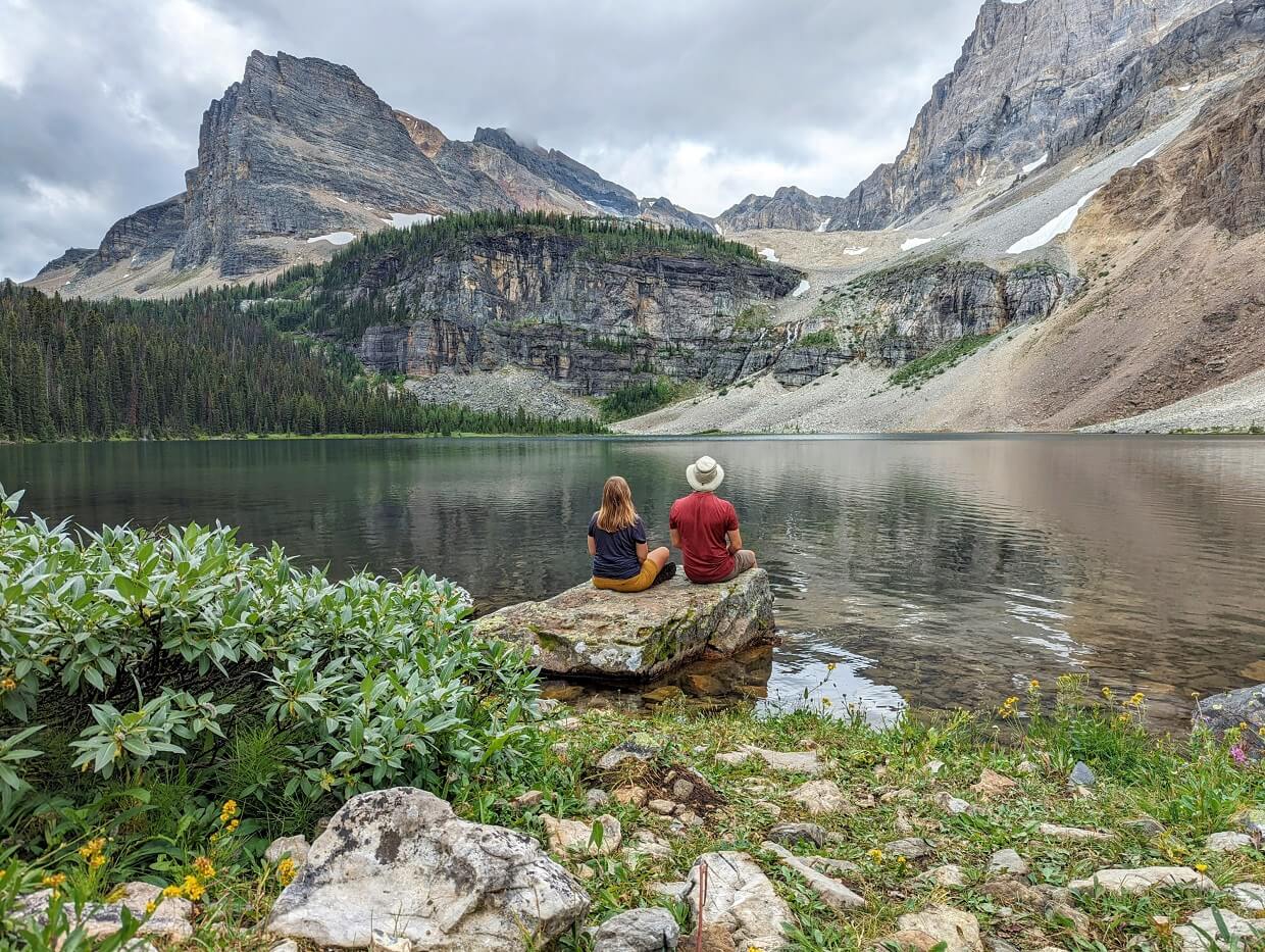 Back view of Gemma and JR sat on rock next to Haiduk Lake, which is very calm and reflecting the mountains above