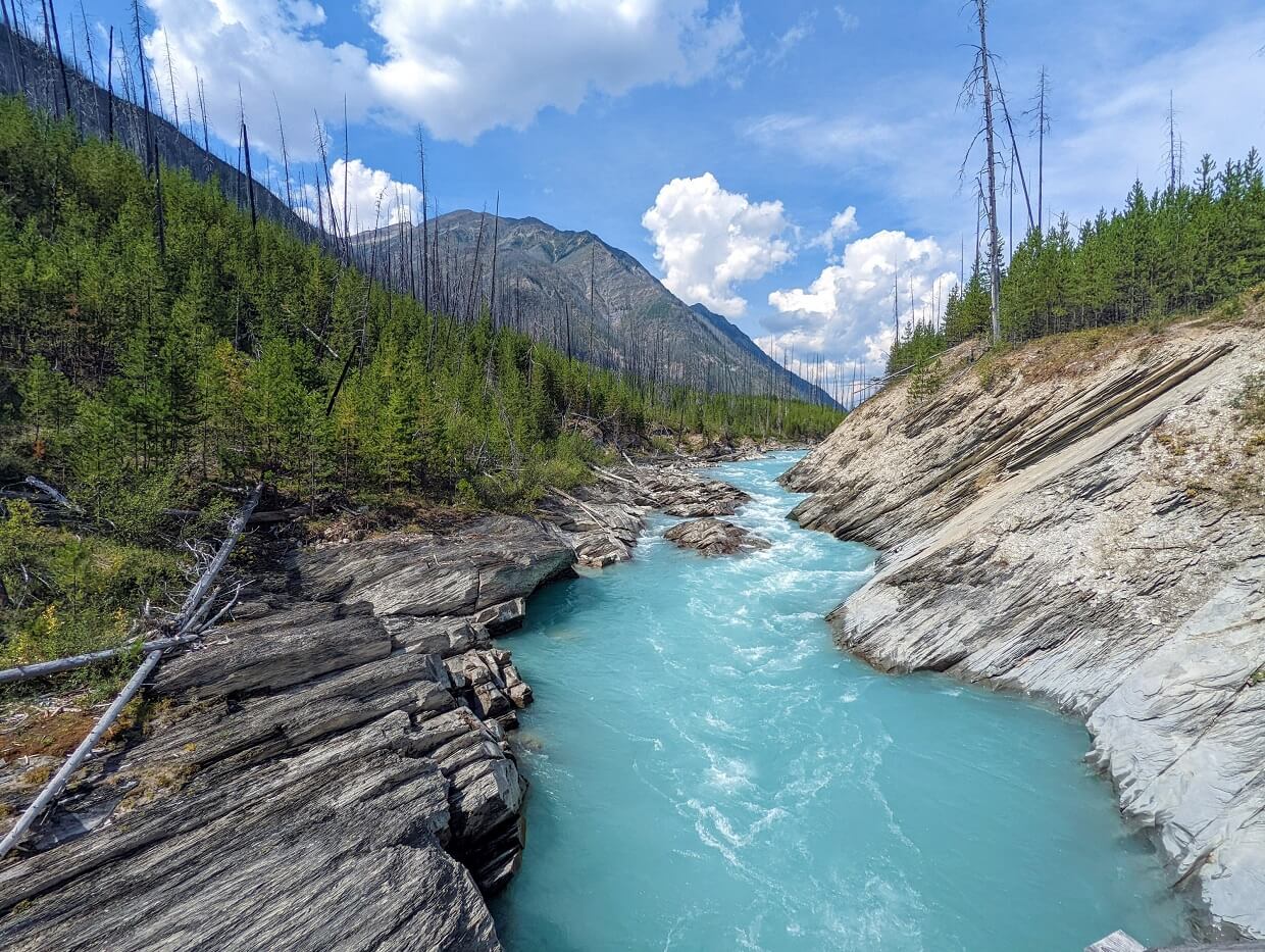 Bright cloudy blue coloured river running through rocky gorge with trees on either side and mountain in background