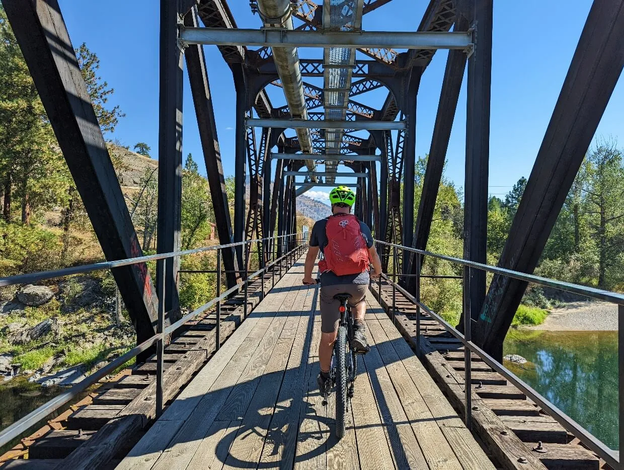 Back view of JR cycling through steel trestle bridge on Columbia and Western Rail Trail