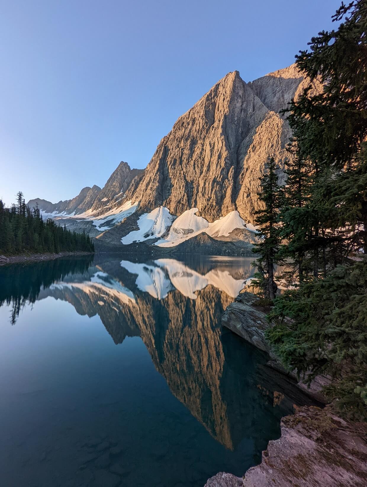 Snow capped mountain reflections on calm Floe Lake, with trees on either side