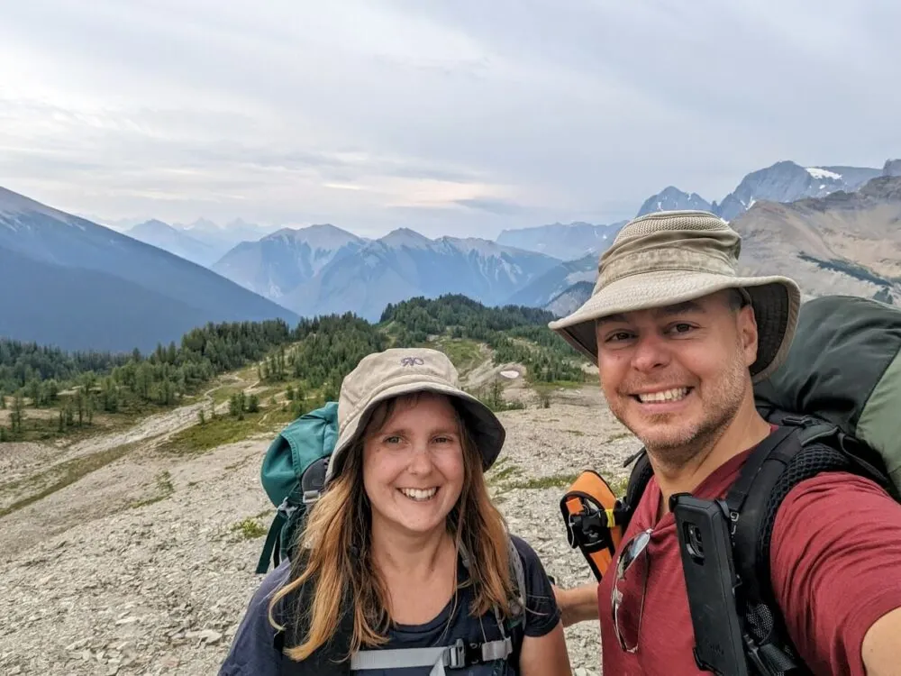 Selfie of JR and Gemma on the Great Divide Trail, both carrying large backpacks in mountainous area