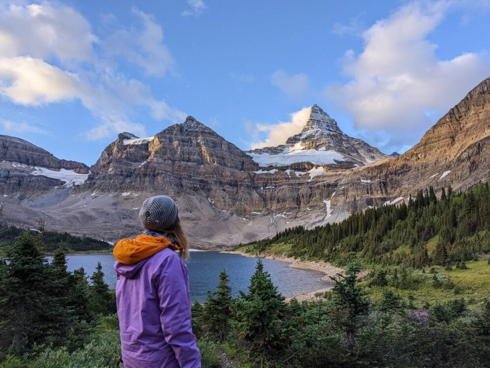 Back view of Gemma looking towards the diamond shaped snow capped peak of Mount Assiniboine, with Lake Magog at the base 