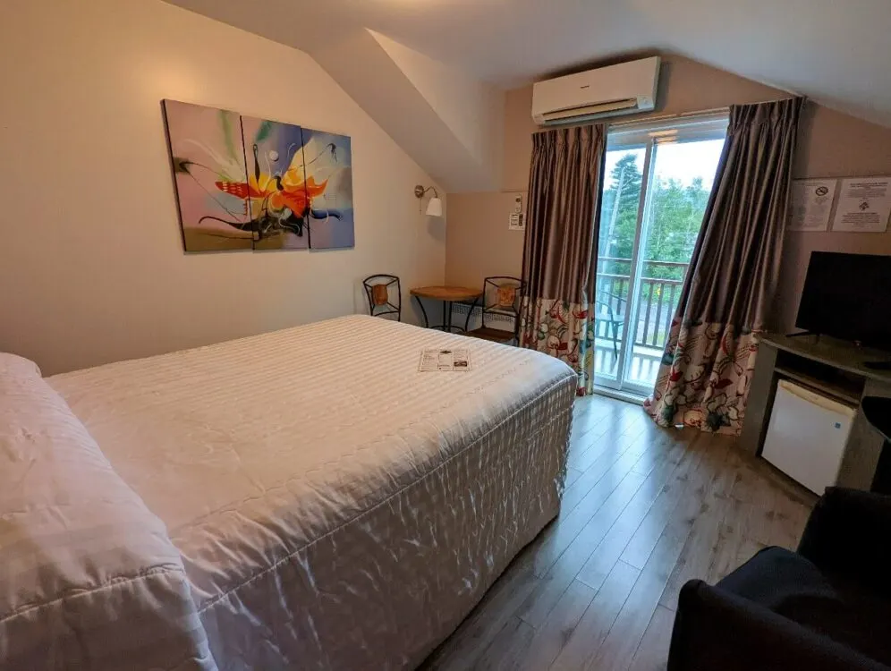 Wide angle view of hotel room with queen bed, table and chairs, television, fridge and patio doors