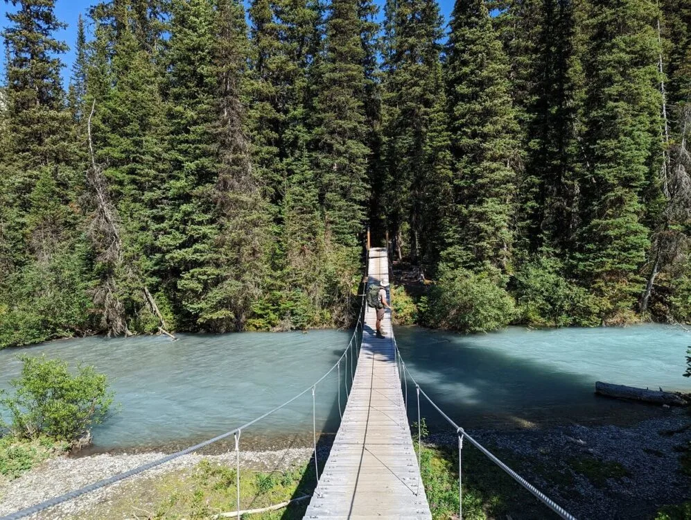 Side view of JR standing on suspension bridge over cloudy blue river on the Rockwall Trail