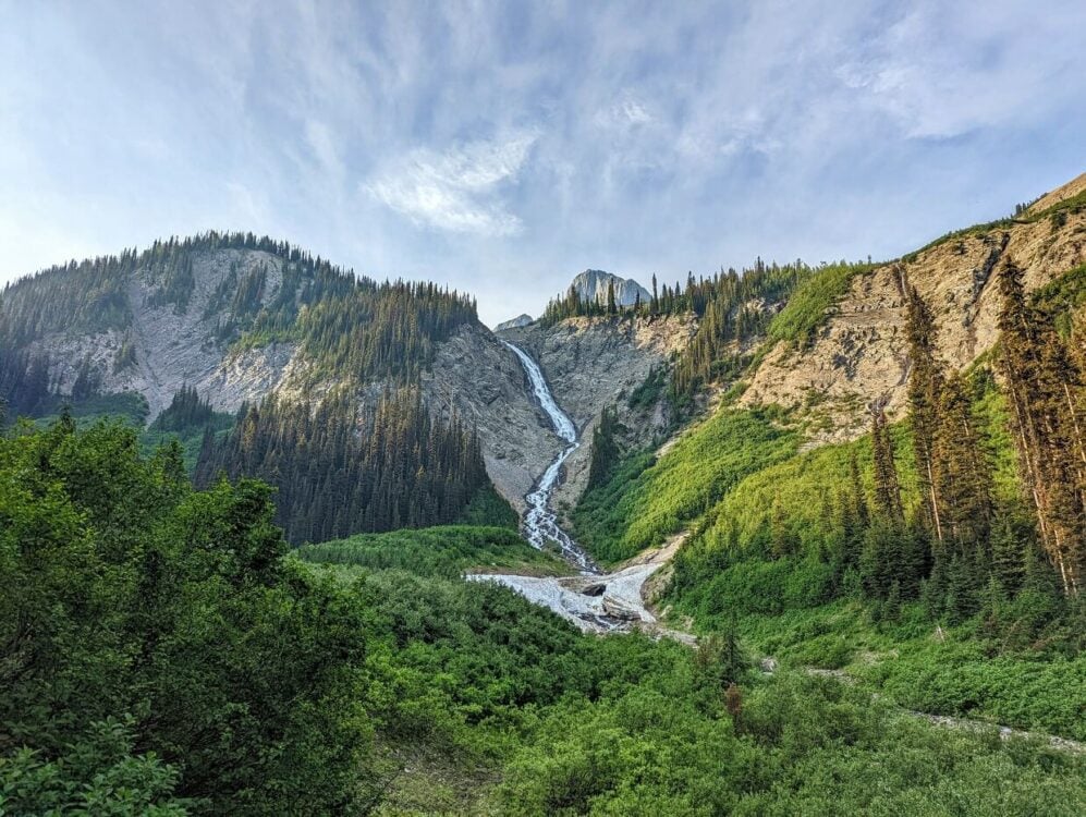 Looking up to large waterfall cascading down rock face, surrounde by forest