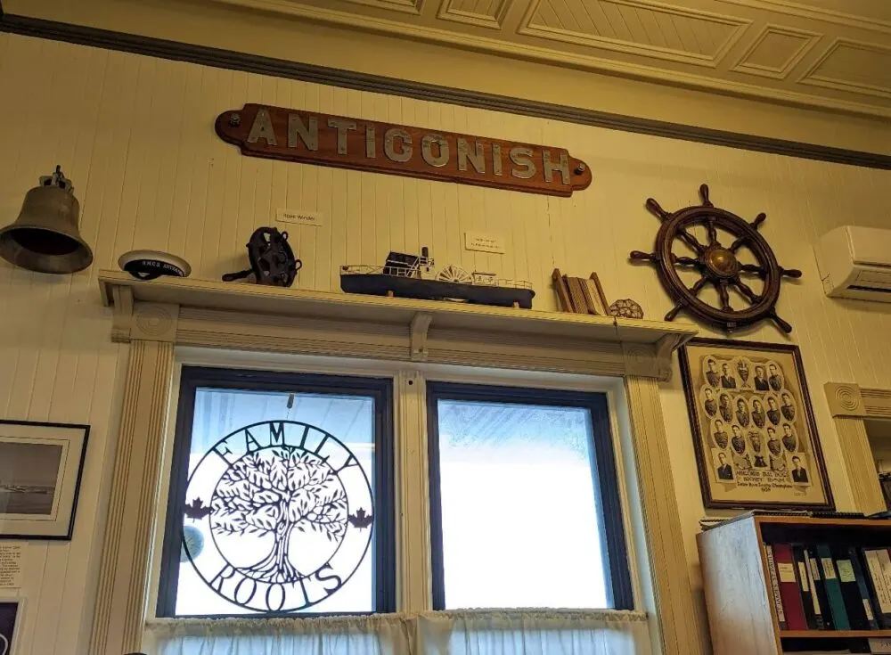 Interior view of museum with Antigonish railway sign near ceiling, boat wheel and genealogy information on walls