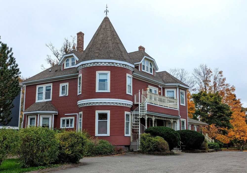 Exterior view of Antigonish Victorian Inn - three story historic building with turret and exterior spiral staircase. Trees in background with autumnal colours