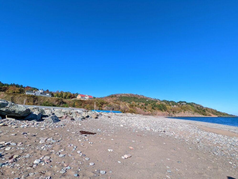 Looking across rock and sand beach at Ballantyne's Cove with houses and headland/hills visible in background