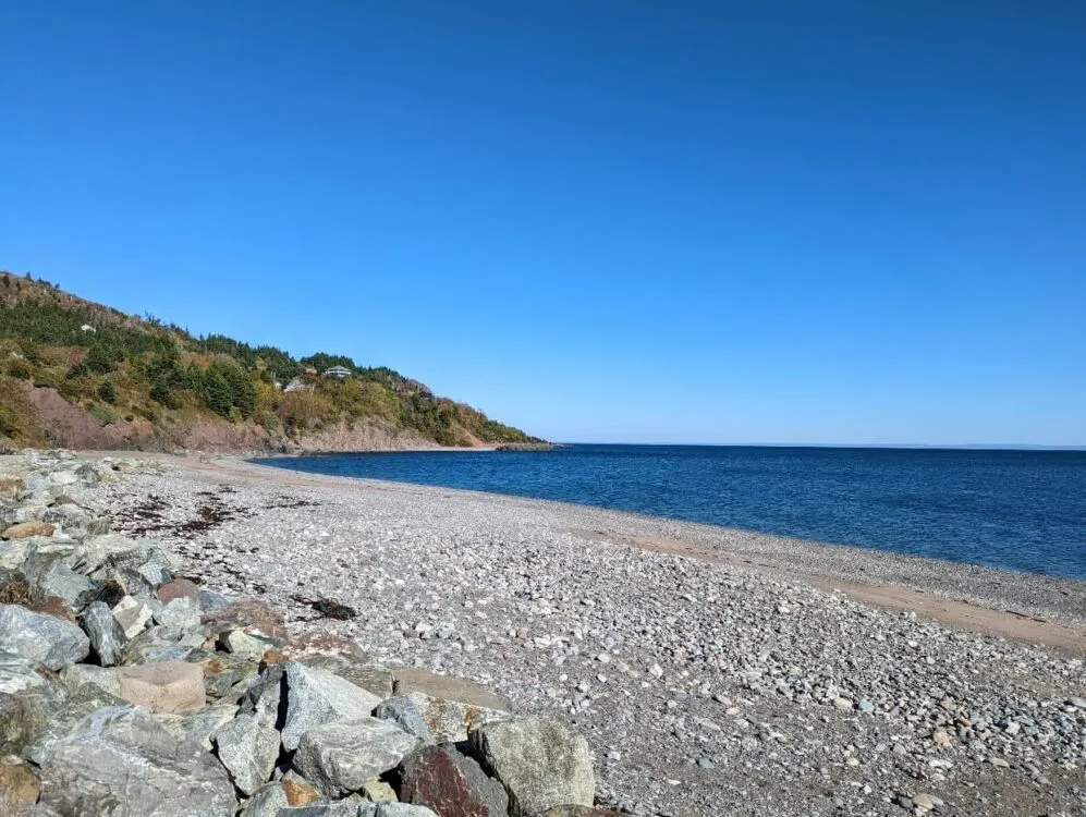 Looking across rocky and sand beach at Ballantyne's Cove with calm ocean and headland behind