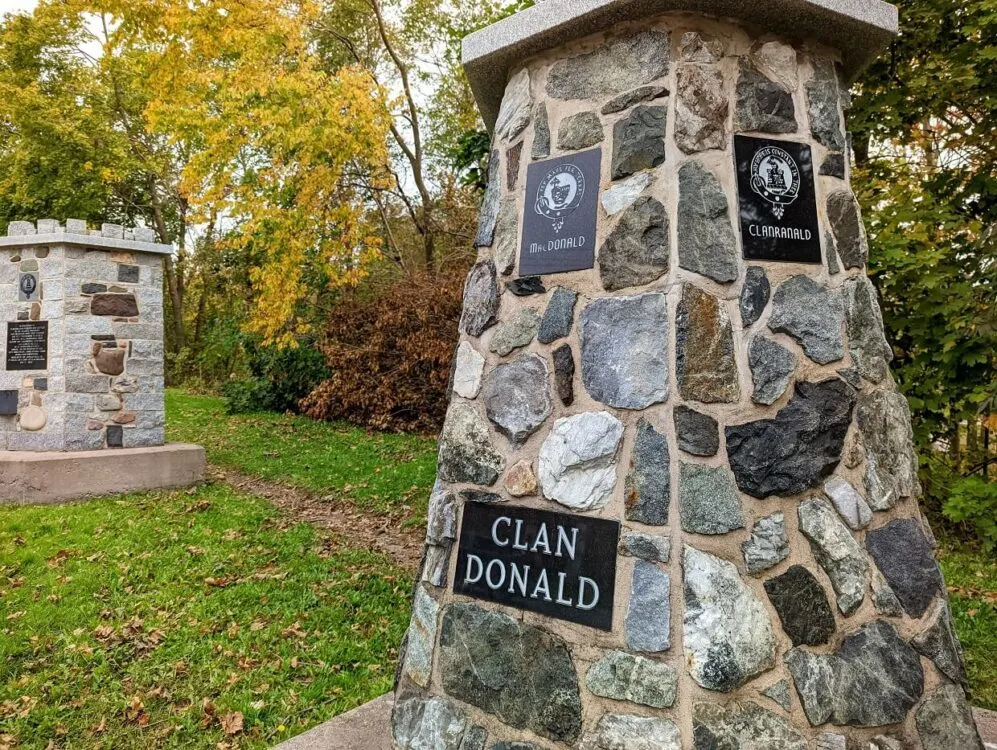 Close up of stone cairn with Clan Donald signs on it in Cairn Park in Antigonish, Nova Scotia. Trees are visible in the background, some already turned golden