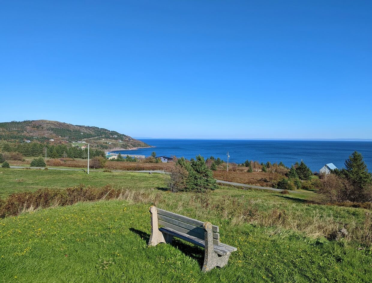 Back view of bench in front of coastline on Cape George Scenic Drive, with calm ocean in background